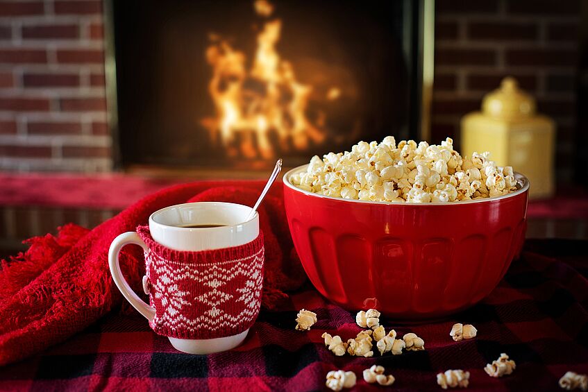 Eine Tasse und eine Schüssel Popcorn vor einem Feuer im Kamin