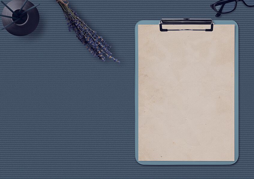 Ein leeres Blatt Papier auf einem Klemmbret, daneben eine Schreibfeder.